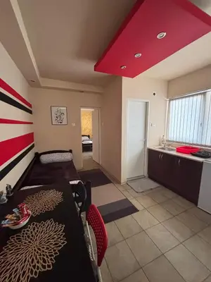 a room with a bed and a table and a kitchen at Dody Apartmani in Leskovac