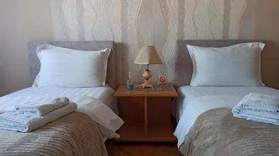 two beds with white sheets and a night stand with a lamp at Community Park Apartment in Niš