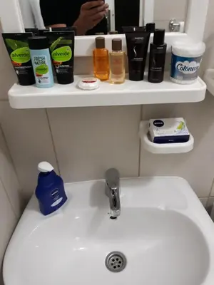 a bathroom sink with hygiene items on shelves above it at Stan Na Dan in Niš