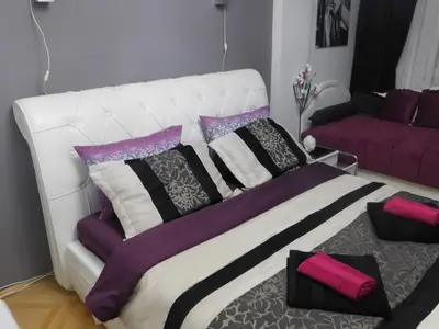 a white bed with purple and black pillows in a room at Velvet Lux in Niš