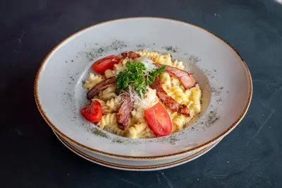 a bowl of pasta with bacon tomatoes and cheese at Garni Hotel Lotos in Niš