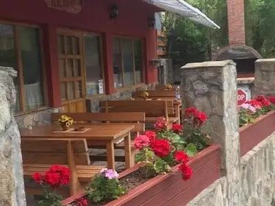 a wooden table and bench on a porch with red flowers at Kod Dace in Banja Topilo