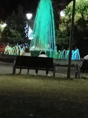 a person sitting on a bench in front of a fountain at night at Nidza Vranjanac in Vrnjačka Banja