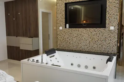 a bathroom with a tub with a tv on the wall at Princ Apartment in Niš