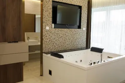 a bathroom with a large tub with a tv on the wall at Princ Apartment in Niš