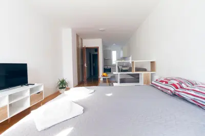 a white bedroom with a large bed and a flat screen tv at Tea Studio Apartments in Niš