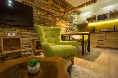 a living room with a stone wall and two green chairs at Family Apartmani Kopaonik in Kopaonik