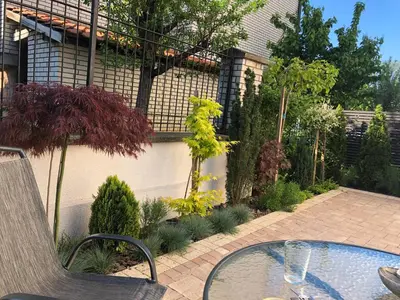 a patio with a glass table in a garden at Vrnjacka Idila in Vrnjačka Banja
