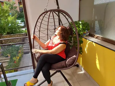 a woman sitting in a swing chair looking out a window at Guest House Pavlovic in Soko Banja