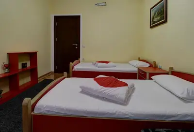 two beds in a room with two tables and a door at PERLA Leskovac in Leskovac
