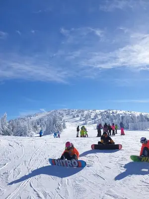 a group of people sitting in the snow with snowboards at Neva Apartment Angella Konaci in Kopaonik