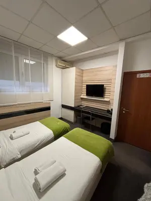 two beds in a room with a desk and a television at Garni Hotel Consul in Niš