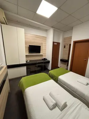 a room with two beds and a desk with a television at Garni Hotel Consul in Niš