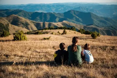 three people sitting in a field looking at mountains at Hotel Kraljevi Čardaci in Kopaonik