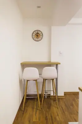 two white stools under a table in a room with a clock at NEW Center Apartments in Niš