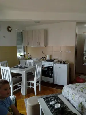 a small kitchen with a table and a child sitting on a chair at Агни in Vrnjačka Banja