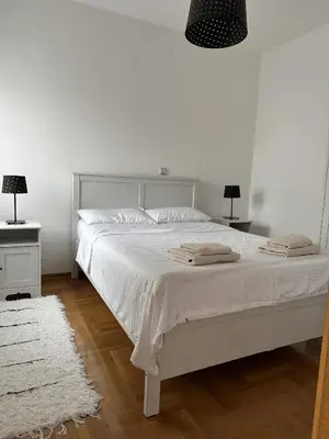 a white bedroom with a white bed with two lamps at Apartment Matovic in Vrnjačka Banja