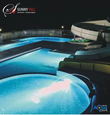 a swimming pool with blue water at night at Sunny Hill Apartments & Aqua Park in Vrnjačka Banja