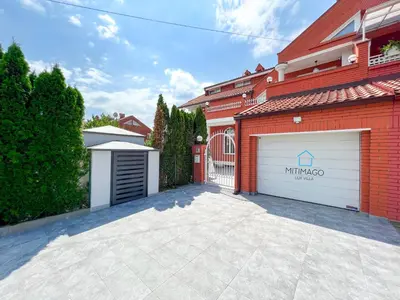 a garage with two white garage doors and a red building at Lux Villa Mitimago in Niš