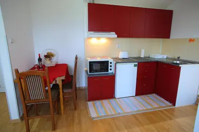 a kitchen with red cabinets and a table with a microwave at Apartmani Djokić sa bazenom in Soko Banja