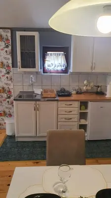a kitchen with white cabinets and a table with a wine glass at Kum Apartment in Niš