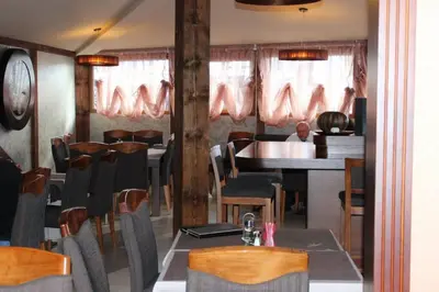 a restaurant with tables and chairs and a man sitting at a counter at Lila Apartman u Kraljevim Čardacima in Kopaonik
