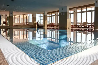a swimming pool with a blue tiled floor and windows at Milmari Resort & Spa Suites in Kopaonik