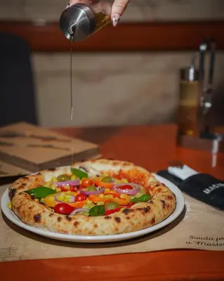 a pizza sitting on top of a table with a person pouring sauce at Apartman Downtown in Vrnjačka Banja