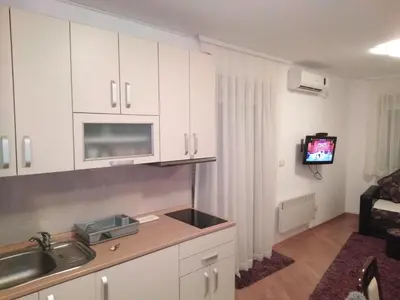 a kitchen with white cabinets and a tv in a room at FEEL LIKE HOME in Vrnjačka Banja
