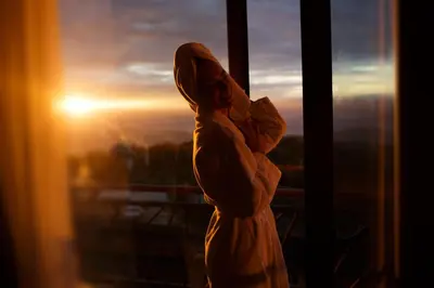 a woman in a robe standing in front of a window at Harmonija Resort - Harmonija Kopaonik in Kopaonik