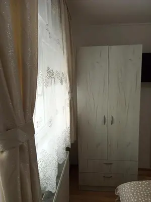 a bedroom with a white curtain and a cabinet at Lili apartman u parku in Vrnjačka Banja