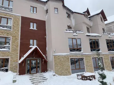 a building with snow on the ground in front of it at Mount Apartments Milmari in Kopaonik