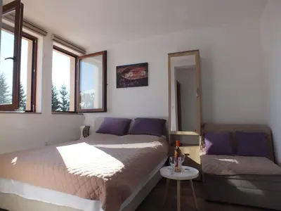 a bedroom with a bed and a couch and windows at SUNCANI BREG - STUDIO 11 in Kopaonik