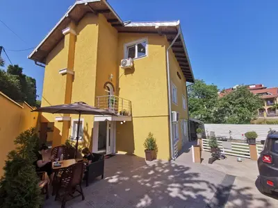 a yellow house with a table and an umbrella at Comfort Inn Apartmani in Vrnjačka Banja