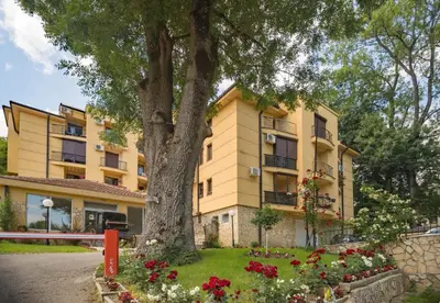 a large yellow building with a tree and flowers at Apartman Modena Lux in Vrnjačka Banja