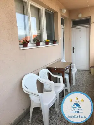 a patio with white chairs and a table and windows at Don in Vrnjačka Banja
