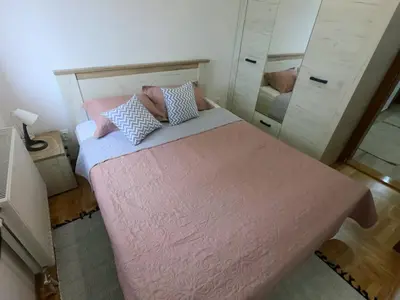 a bedroom with a bed with pink sheets and a mirror at Apartman OAZA in Vrnjačka Banja