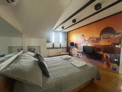 a bedroom with a bed with a painting on the wall at MM Apartman in Kruševac