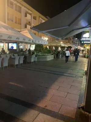a street with tables and chairs and umbrellas at night at Palas Central in Niš