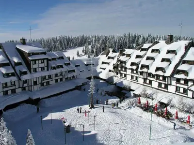 a building covered in snow with people standing in the snow at Megi apartman - Konaci Maglic in Kopaonik