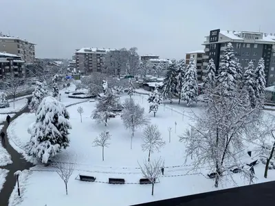 a park covered in snow with trees and buildings at Alo Alo Apartman 6 in Kruševac