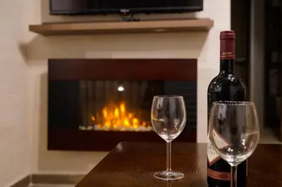 a bottle of wine and two glasses on a table with a fireplace at Vila Rajski kutak Kopaonik in Kopaonik
