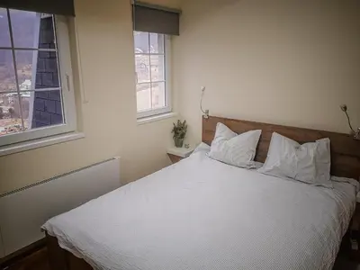 a bedroom with a bed with white sheets and two windows at STAR apartman Brzece Kopaonik in Brzeće