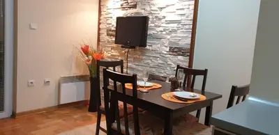 a dining room table with chairs and a tv on a stone wall at Apartman Nikola- 4 ZVEZDICE minimalno 3 nocenja za rezervaciju in Vrnjačka Banja