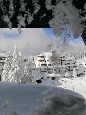 a building covered in snow with trees in the background at Apartman SREBRNA PAHULjA-Konaci in Kopaonik