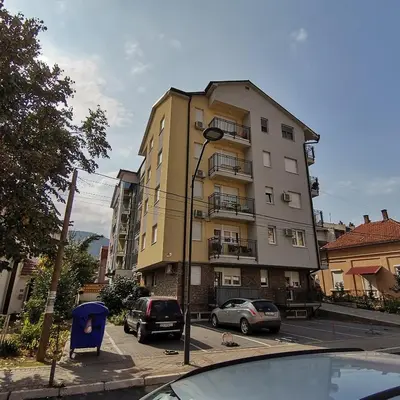 a tall yellow building with cars parked in a parking lot at Apartman Lea & parking u garaži in Soko Banja