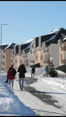 a group of people walking down a snowy street with umbrellas at Suncani breg treska in Kopaonik