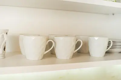 a row of white coffee cups sitting on a shelf at Aparment Theatre in Niš