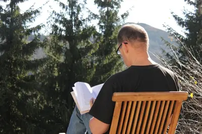a man sitting on a bench reading a book at 4Badgers / 4Jazavca - Mountain House in Kopaonik