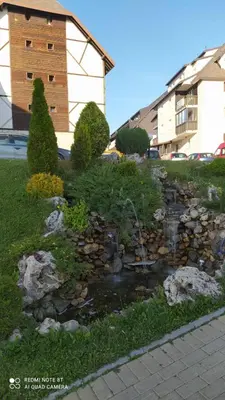 a garden with a creek in front of a building at Apartman Milmari Idila in Kopaonik